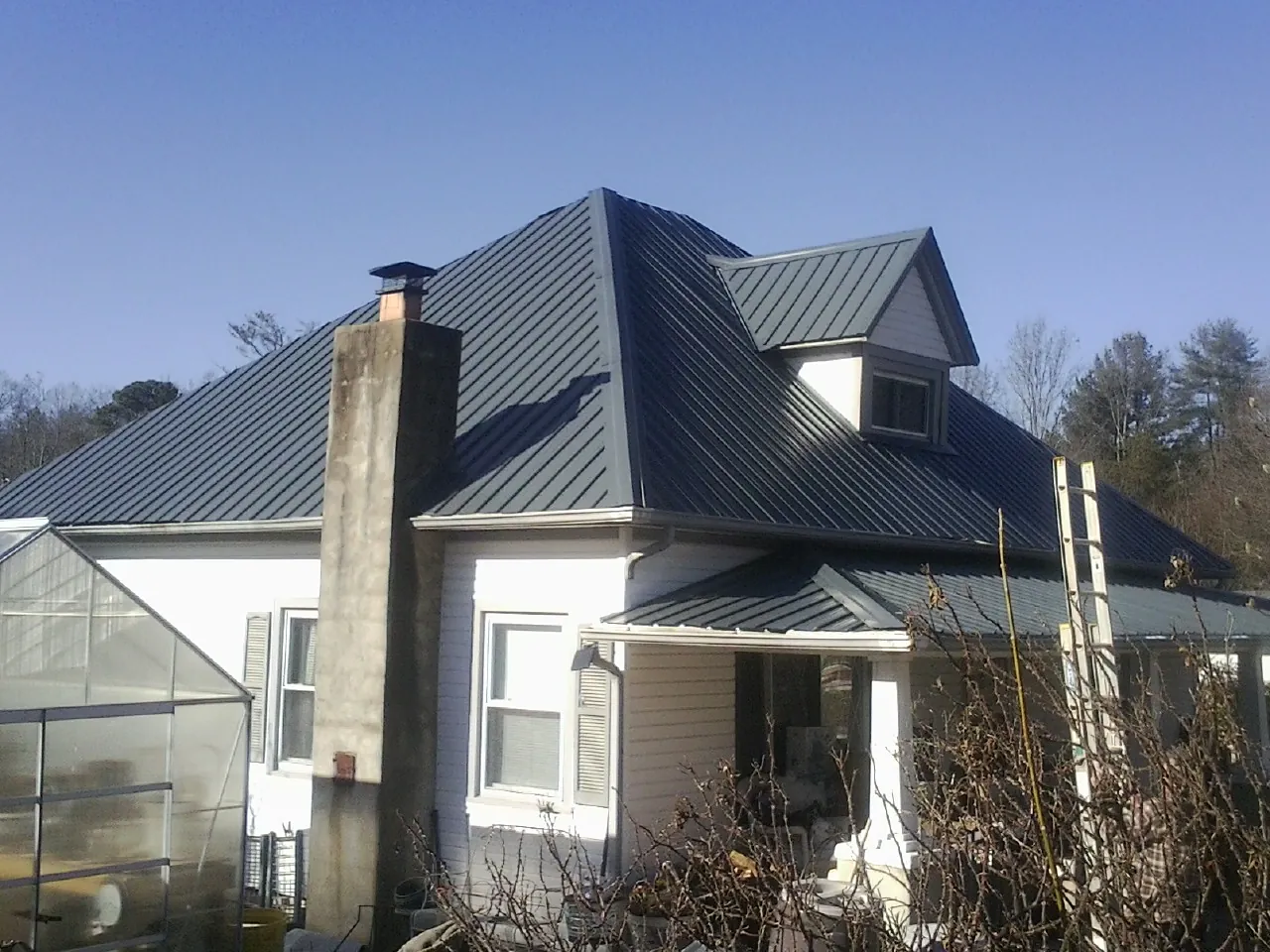 Dark blue standing seam metal roof on a white farmhouse with dormer — Slate & Tile Roof Repair by Roofing Brothers in Blockton