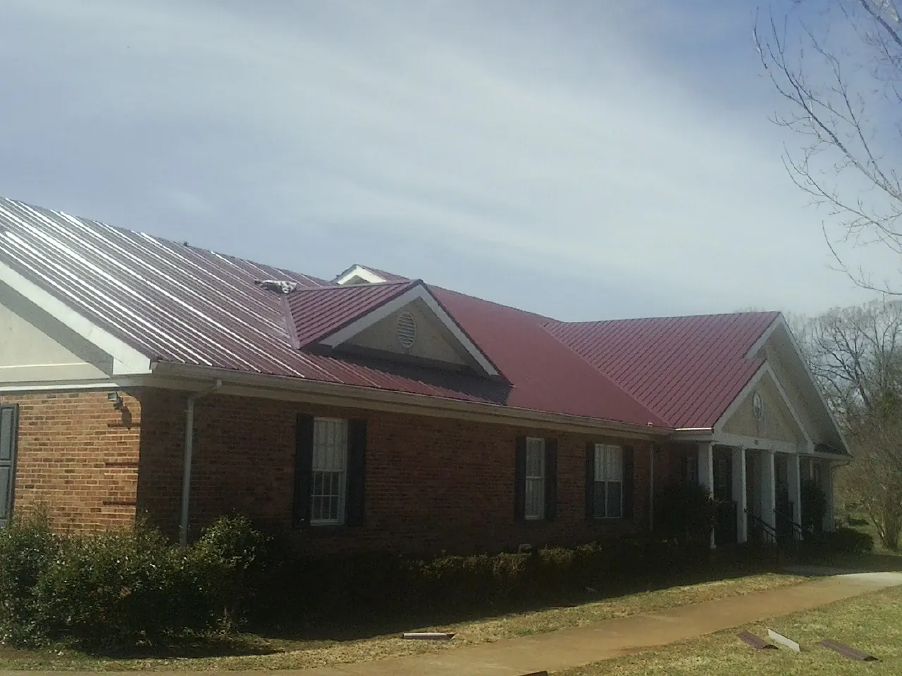 Red metal roof with gabled entries on a long brick building, from a Hail Damage Roof Repair job in Blockton