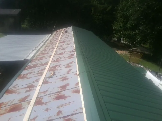 Old rusted panels beside newly installed green metal roofing — Wind Damage Roof Repair by Roofing Brothers in Blockton