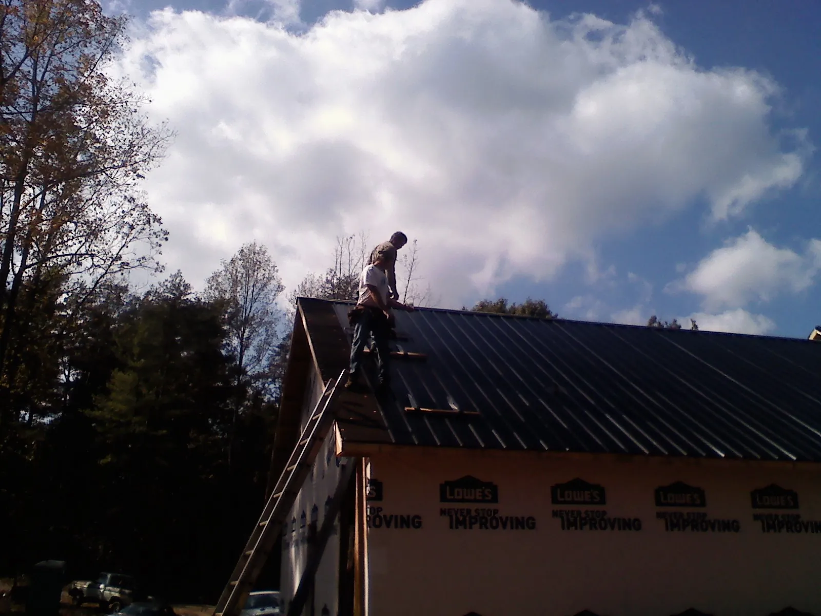 Roofer fastening dark metal panels high against a cloudy sky, from a Roof Inspection job in Blockton