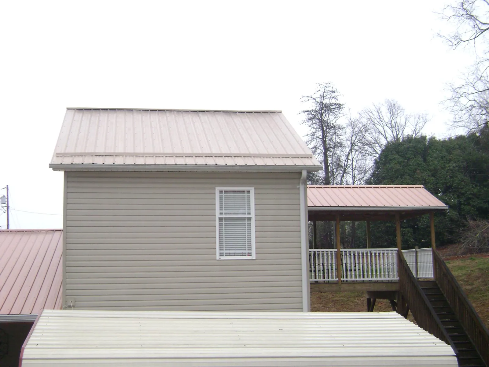 Tan metal roofs on a two story addition and attached porch, from a Roof Replacement job in Blockton